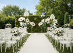 Wedding setup with white chairs, giant floral arrangements, and a clear blue sky.