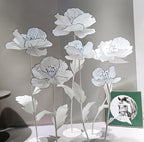 A set of large, white artificial poppy flowers with black illustrated lines, displayed on metal bases.